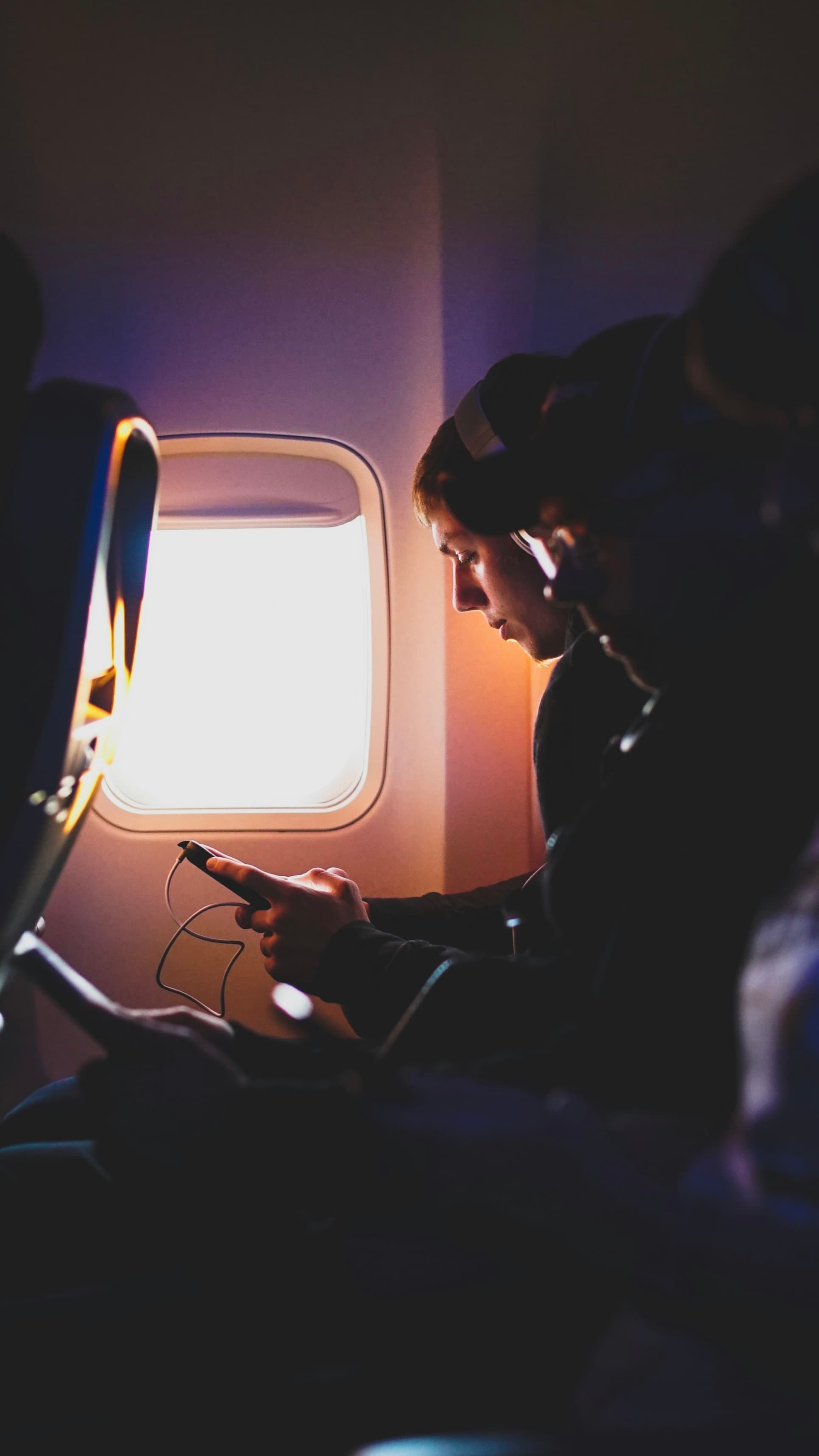 A passenger using a phone while wearing headphones on a plane.